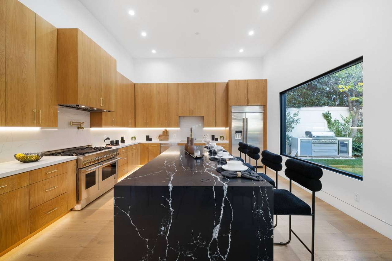 Los Angeles custom kitchen with large black stone island and natural wood cabinetry by Millwork USA